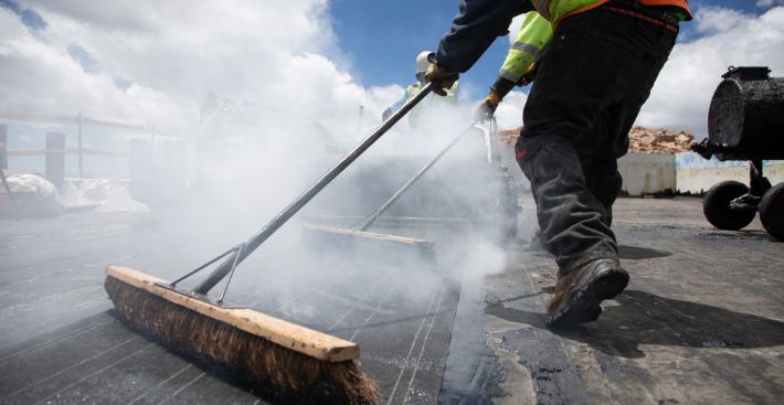 Roll of BUR being broomed into hot asphalt