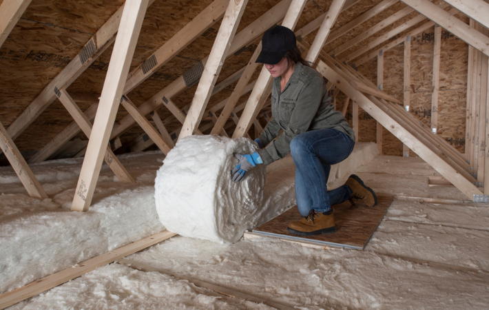 Person installing batt insulation in attic
